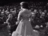 a woman in a long white dress is standing in front of a crowd