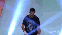 a man in a black shirt with a skull on it is standing in front of a blue light that says aew tnt