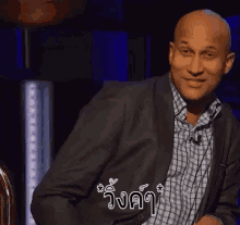 a bald man in a suit and plaid shirt is smiling while sitting in a chair .