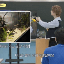 a man stands in front of a blackboard with a picture of an aquarium and a picture of a person holding a yellow object