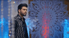 a man with a beard is standing in front of a wall with a pattern on it .