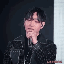 a man in a black jacket is holding a microphone and the name judleklek702 is on the bottom right