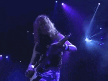 a man with long hair is playing a guitar on stage