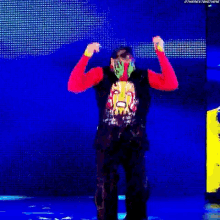 a man in a red shirt and black vest is standing in front of a blue screen .