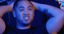 a man with a tattoo on his arm is sitting with his hands behind his head .