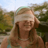 a woman wearing a headband and pearls has her eyes blindfolded