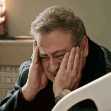 a man with a watch on his wrist covering his face with his hands
