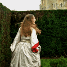a woman in a white dress stands in front of a hedge with a cross on it