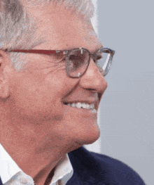 a man wearing glasses and a blue jacket smiles for the camera