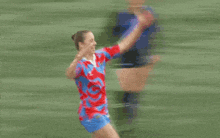 a woman in a red and blue jersey is kicking a soccer ball on a soccer field .