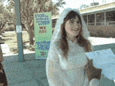 a woman in a wedding dress is holding a piece of paper in front of a sign that says stop spread covid 19 we are together