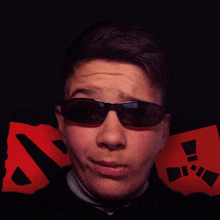 a young man wearing sunglasses stands in front of a red and black logo