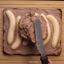 a person is spreading chocolate frosting on a cake with bananas on top