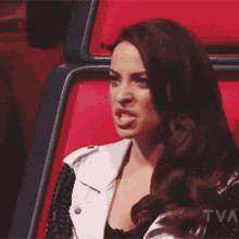 a woman is sitting in a red chair with a tna logo in the background