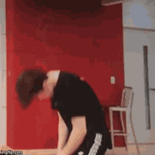 a man is bending over in front of a red wall and a chair .