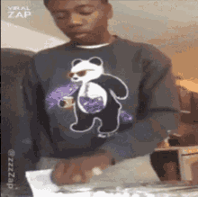 a man wearing a sweater with a panda bear on it is holding a piece of paper