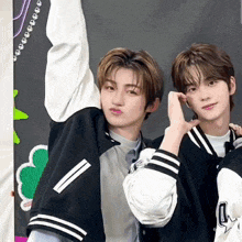 two young men wearing varsity jackets are posing for a picture . one of the jackets has the letter a on it .