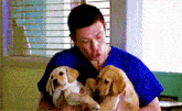 a man in a blue shirt is holding two puppies in his arms .