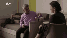 a man in a purple shirt sits next to a woman in a chair with a hd logo on the bottom