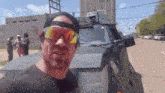 a man wearing sunglasses and a hat is standing in front of a black vehicle .