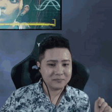 a man wearing headphones and a floral shirt is sitting in a chair in front of a monitor .