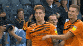 two soccer players wearing orange jerseys with the word sportpesa on them