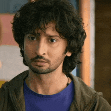 a man with curly hair and a beard is wearing a blue shirt and a brown jacket
