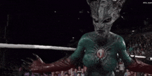 a monster with horns is in a wrestling ring with a crowd behind him