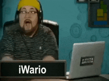 a man wearing headphones is sitting in front of a laptop with the name iwario on the screen