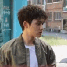a young man wearing a green jacket and a white shirt is standing outside of a building .