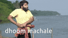 a man in a yellow shirt stands in front of a body of water with the words dhoom machale written on the bottom right