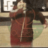 a woman in a red jacket is standing on a basketball court holding a hoop .