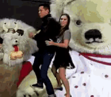 a man and a woman are dancing in front of a giant stuffed polar bear .