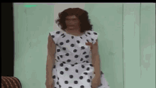 a man in a polka dot dress is standing in front of a couch .