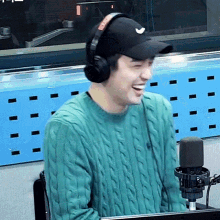 a man wearing headphones and a hat is sitting in front of a microphone and smiling