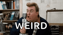 a man is holding a microphone in front of a bookshelf and the word weird is on the screen .