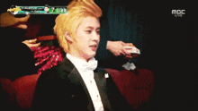 a man in a tuxedo and bow tie is sitting in a theatre watching a live show on mbc