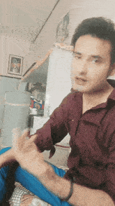 a young man in a maroon shirt is sitting on a bed