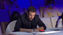 a man wearing a necklace with a cross on it sits at a table with a glass of water