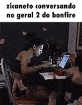 a woman is sitting at a table with a laptop and a fan .