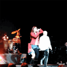 a woman in a red jacket singing into a microphone on stage