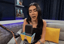 a woman sitting on a couch with a microphone in front of her and a box that has a man on it