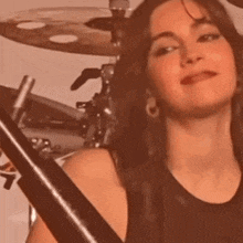 a woman is playing a drum set and smiling while looking at the camera .