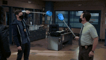a man wearing a mask holds up a blue hand while another man holds a stick