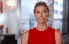 a woman wearing a red top and blue earrings makes a funny face