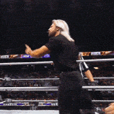 a wrestler in a black shirt is standing in a wrestling ring with a referee .