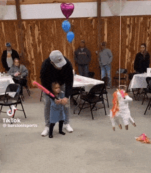 a man is holding a little girl while she plays with a bat and a piñata that looks like a unicorn