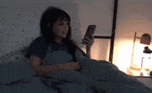 a woman laying in bed looking at her cell phone