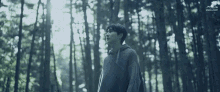 a man in a sweater is standing in a forest looking up at the sky .
