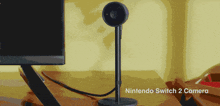a nintendo switch 2 camera sits on a desk next to a monitor